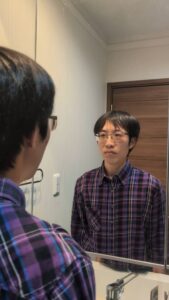 鏡に向かって笑顔練習する男性