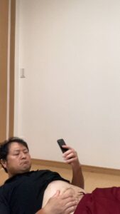 お腹を出してスマホを操作する男性｜お腹｜スマホ