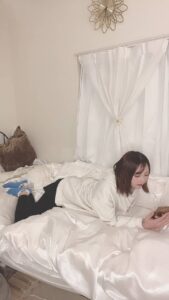 ベッドで寝転んでスマホを見る女性｜日常