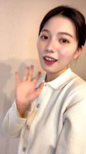 カメラに軽く手を振る女性｜笑顔｜手を振る